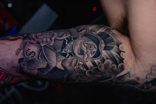 Black and grey upper-arm tattoo of a pre-Hispanic warrior profile with a feathered headdress