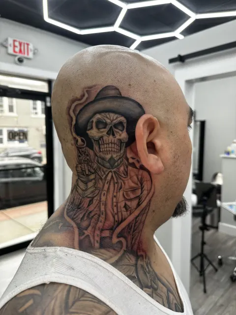 Black and grey neck tattoo of a skull wearing a charro hat, set behind the ear