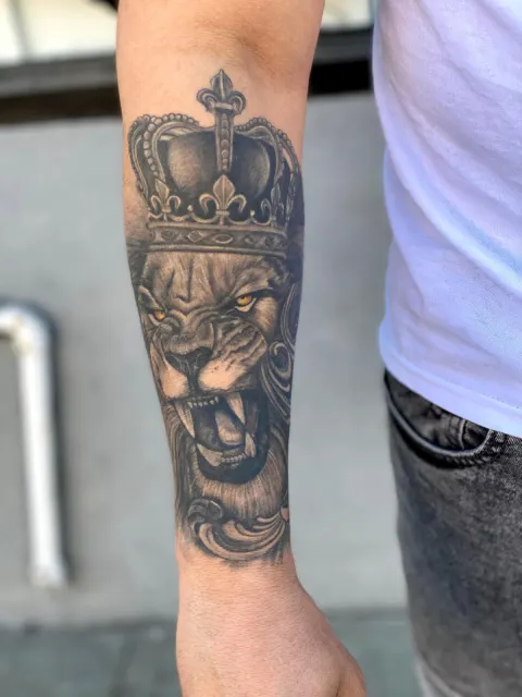 Black and grey forearm tattoo of a roaring lion wearing a crown