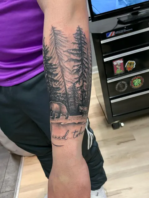 Black and grey forearm band of a pine forest with a walking bear over script