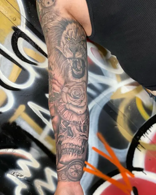 Black and grey full sleeve of a lion, roses, a skull and a compass