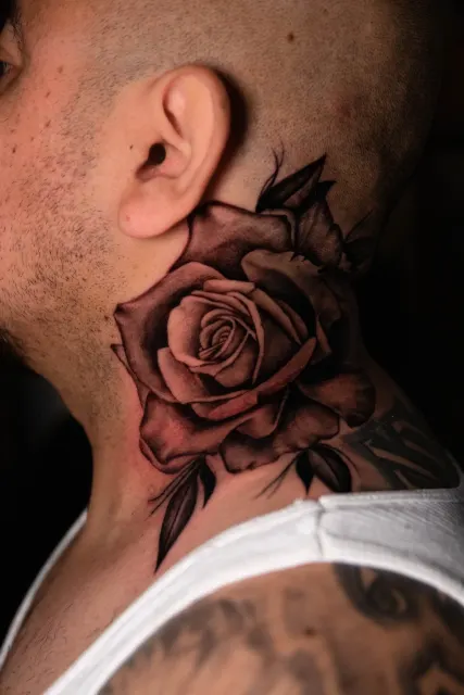 Black and grey rose tattooed on the side of the neck with a leafed stem