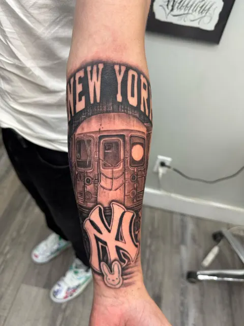 Black and grey forearm tattoo of a subway car under New York lettering with the Yankees mark