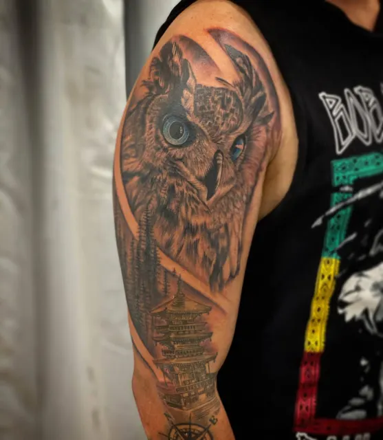 Black and grey shoulder tattoo of an owl watching over a city skyline with dice