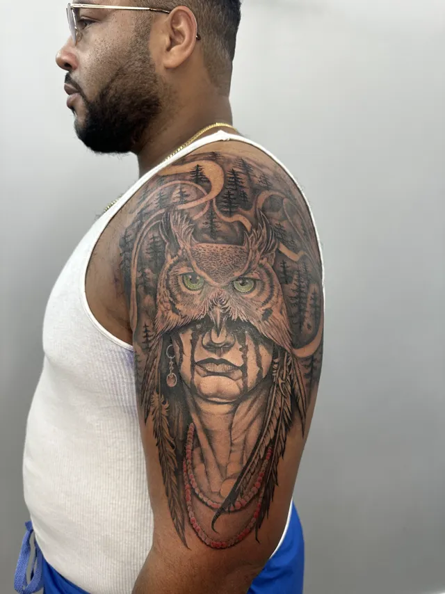 Black and grey shoulder tattoo of a woman wearing an owl headdress
