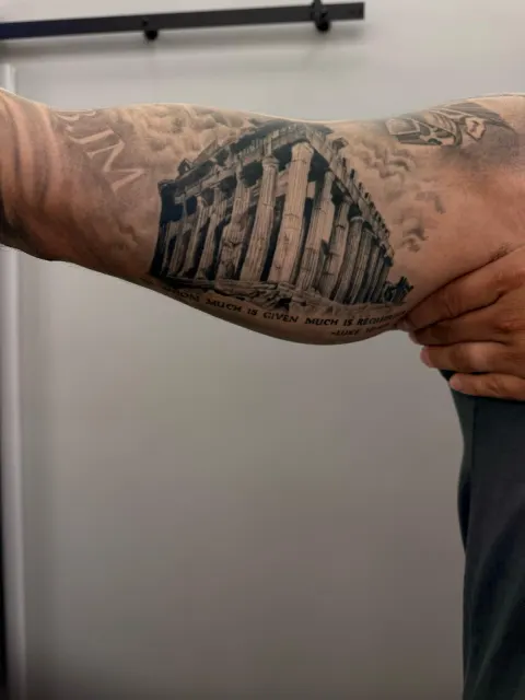 Black and grey inner-arm tattoo of the Parthenon in clouds