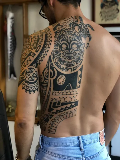 Blackwork shoulder and back panel of Polynesian patterns around a central tiki face
