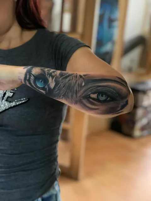 Inner-forearm tattoo pairing a wolf with a realistic blue eye