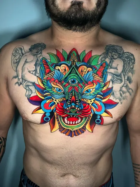 Color chest tattoo of a Balinese barong mask in layered red, green and blue geometry