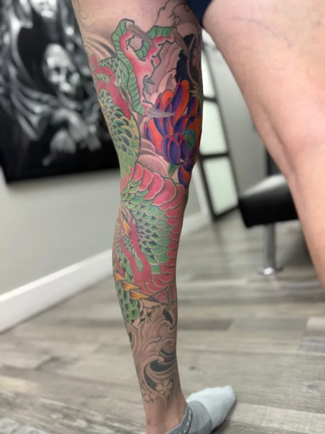 Full-leg color tattoo of a serpent winding through chrysanthemums and finger waves
