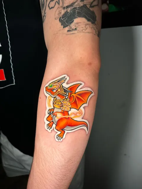 Color elbow tattoo of an orange cartoon dragon rendered as a die-cut sticker