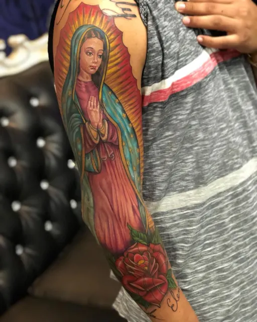 Color upper-arm tattoo of the Virgin of Guadalupe with a red rose below