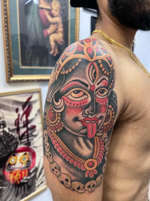 Color shoulder tattoo of the goddess Kali with a red face, extended tongue and a necklace of skulls
