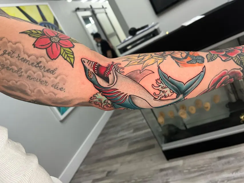 Color arm tattoo of a koi swimming through teal leaves and pink blossoms