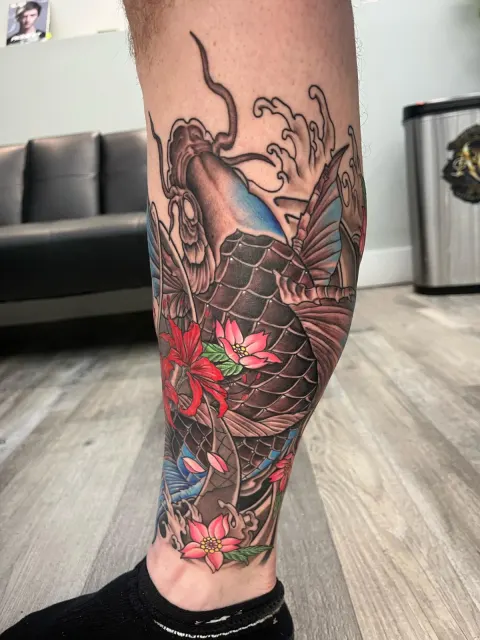 Color calf tattoo of a koi diving through waves toward pink lotus flowers