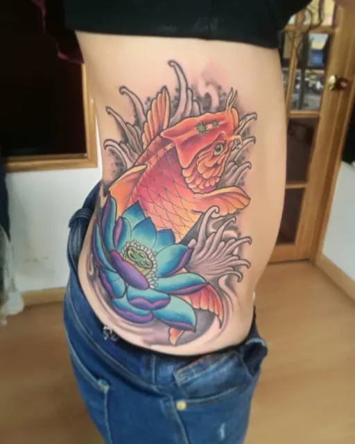 Color rib tattoo of an orange koi over a blue lotus in watercolor washes