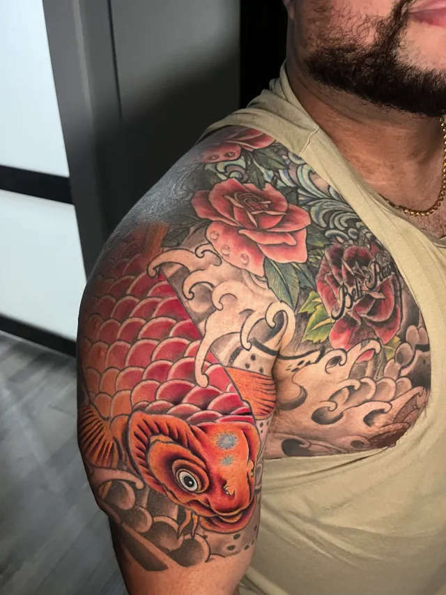 Color shoulder and upper-arm tattoo with a red-orange koi, red roses, green leaves, and stylized waves
