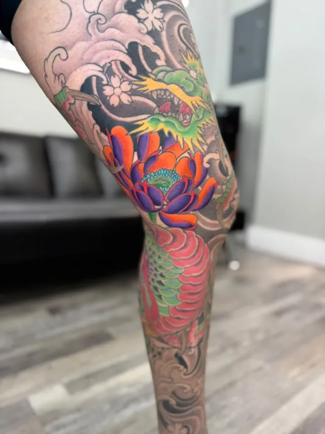 Color tattoo of a purple and orange peony over the knee beneath a green dragon head