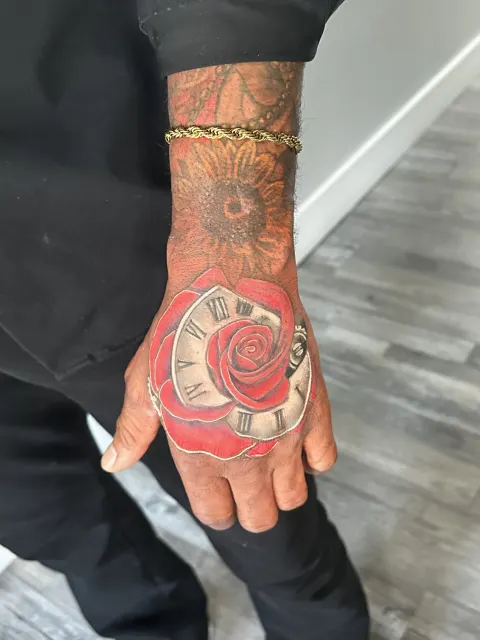 Color hand tattoo of a clock face crowned by a red rose
