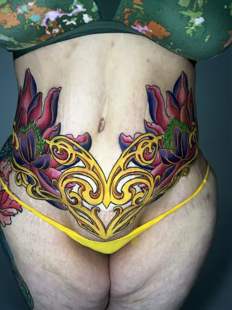 Ornamental color tattoo of gold filigree and leaves across the lower waist