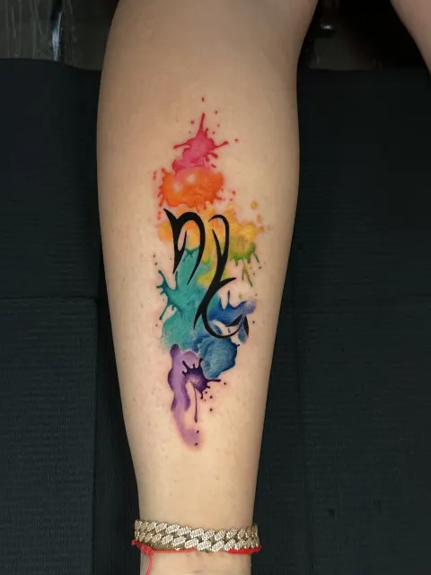 Forearm tattoo of a hummingbird over violet and teal watercolor splashes
