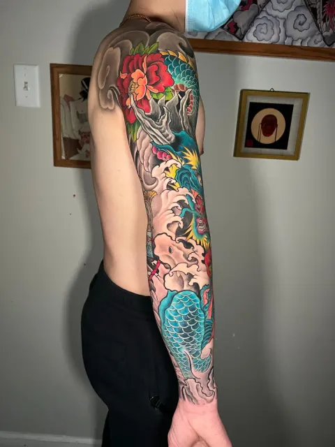 Neo-Oriental full sleeve of a blue dragon descending through red blossoms and waves