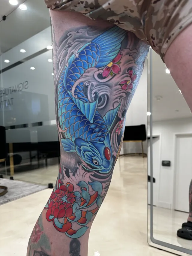 Neo-Oriental tattoo of a blue koi with red floral accents