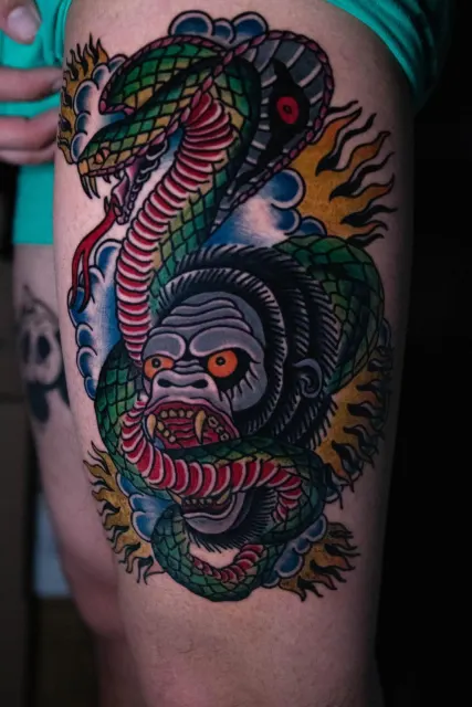 Neo-Oriental thigh tattoo of a green dragon coiled around an ape face over flames