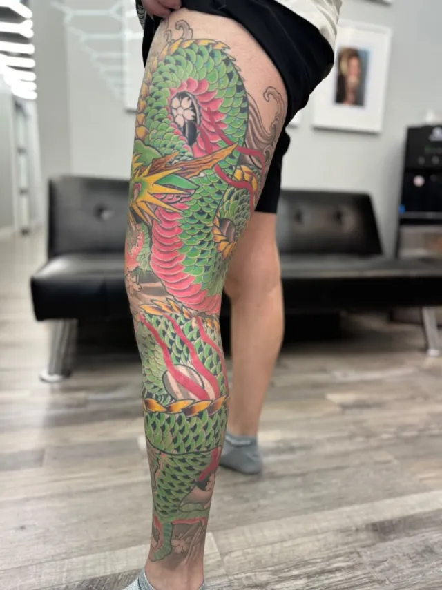 Full-leg neo-oriental tattoo of a green dragon coiled from thigh to ankle with a sunflower core