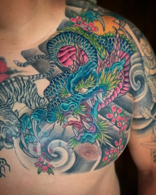 Neo-Oriental chest and shoulder tattoo where a teal dragon meets a tiger among waves and blossoms