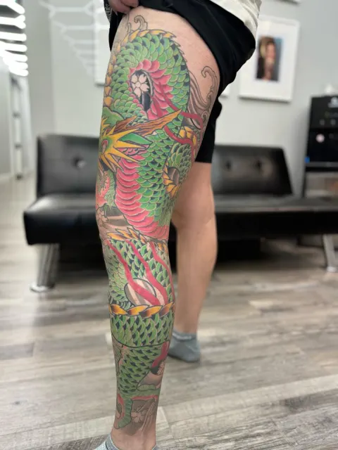 Full-leg neo-oriental tattoo of a green scaled serpent winding from thigh to ankle