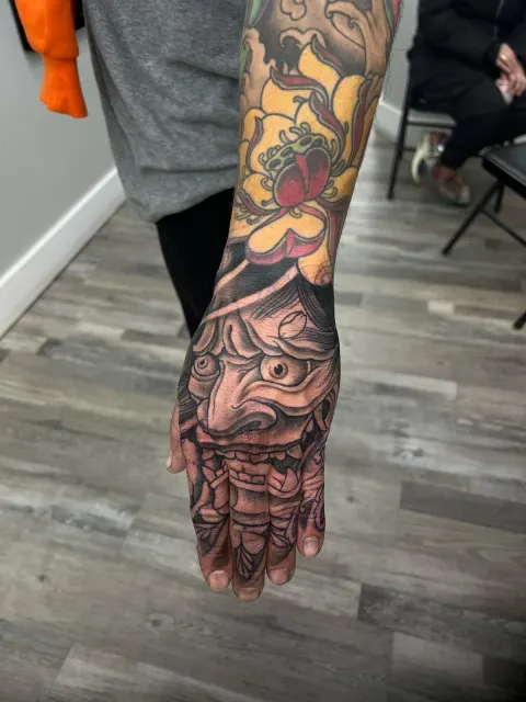 Hannya mask tattooed across the back of the hand and fingers in muted grey and red