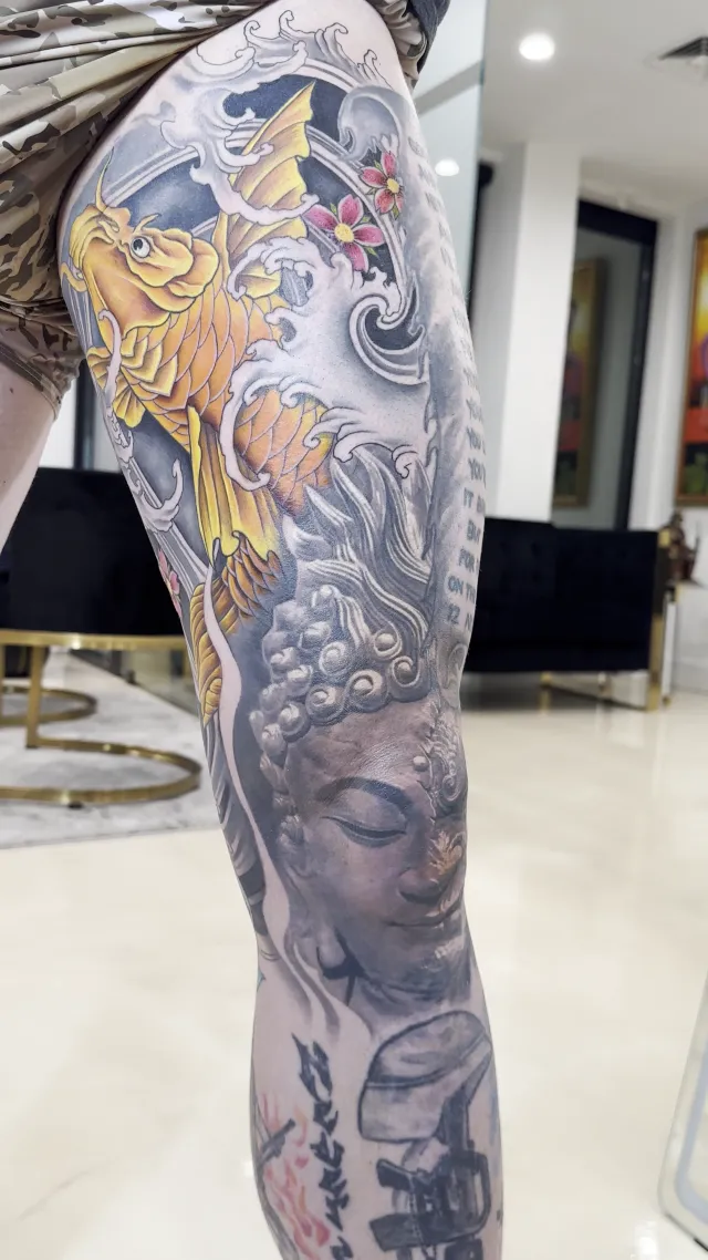 Full-leg neo-oriental tattoo pairing a golden koi in windbars with a black and grey Buddha head