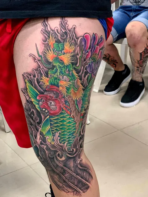 Neo-Oriental thigh tattoo of a green koi in flames beside a warrior mask