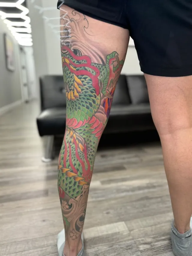Full-leg neo-oriental tattoo of a phoenix with layered green plumage and flame tails