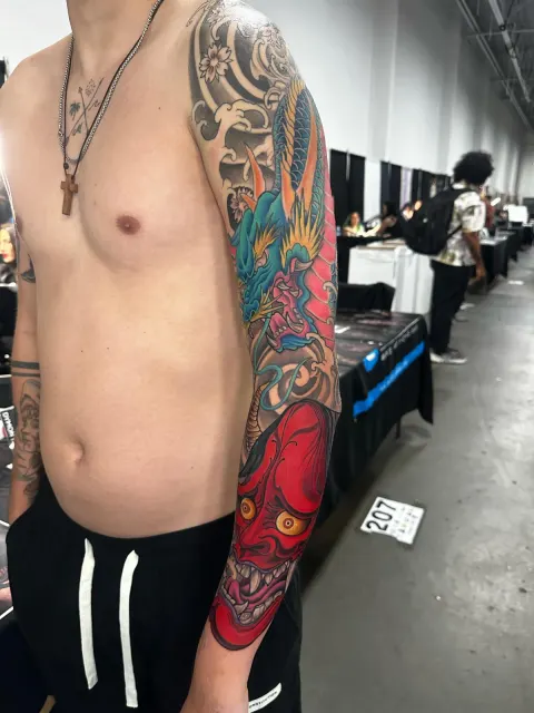 Neo-Oriental full sleeve carried by a red hannya mask on the forearm, photographed at a tattoo convention