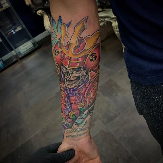 Neo-Oriental forearm tattoo of a horned samurai helmet and mask in red and gold