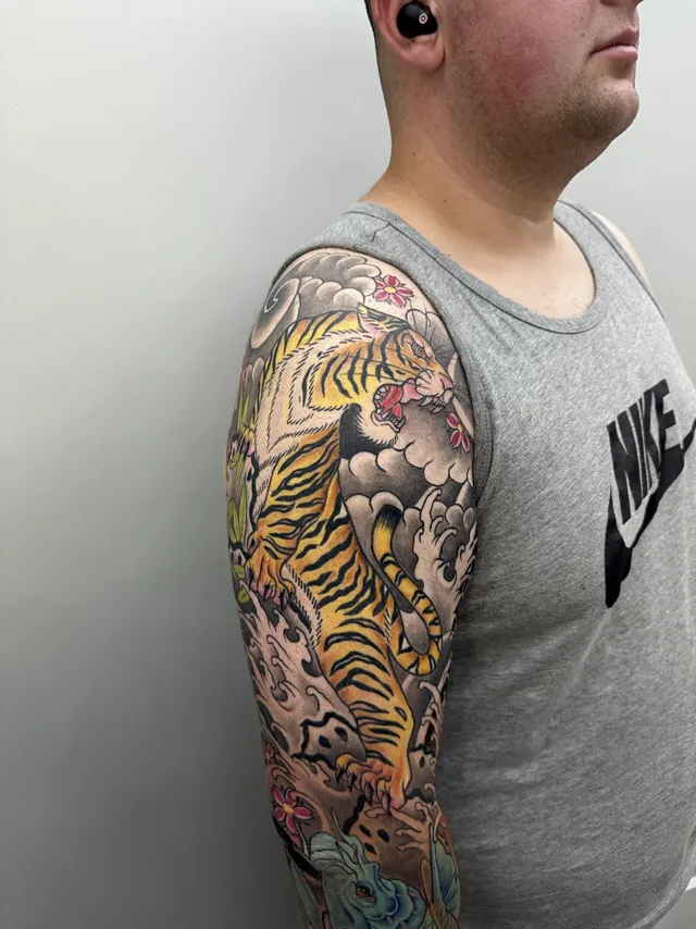 Neo-Oriental full sleeve of a tiger moving through waves, clouds, and red blossoms