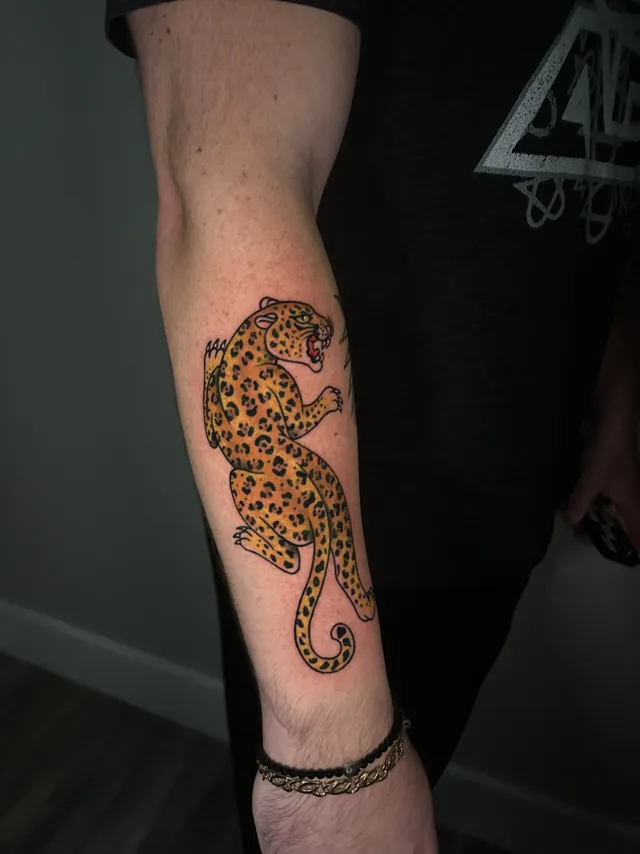 Traditional tattoo of a crawling spotted leopard on the forearm