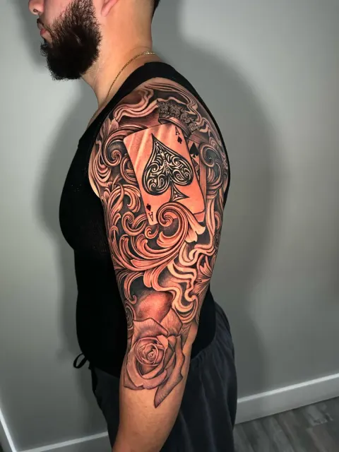 Ornamental upper-arm tattoo of an ace of spades over filigree and a rose
